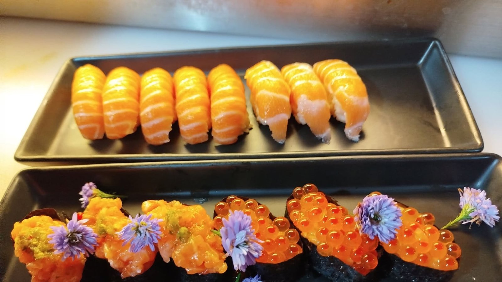 Salmon nigiri and ikura gunkan plated on black trays at the Nigi Express counter